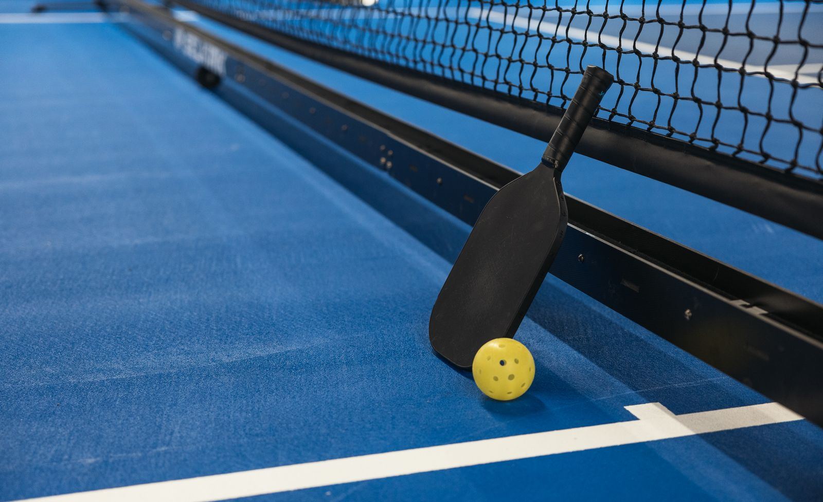 Pickleball paddle and perforated yellow ball beside a court net